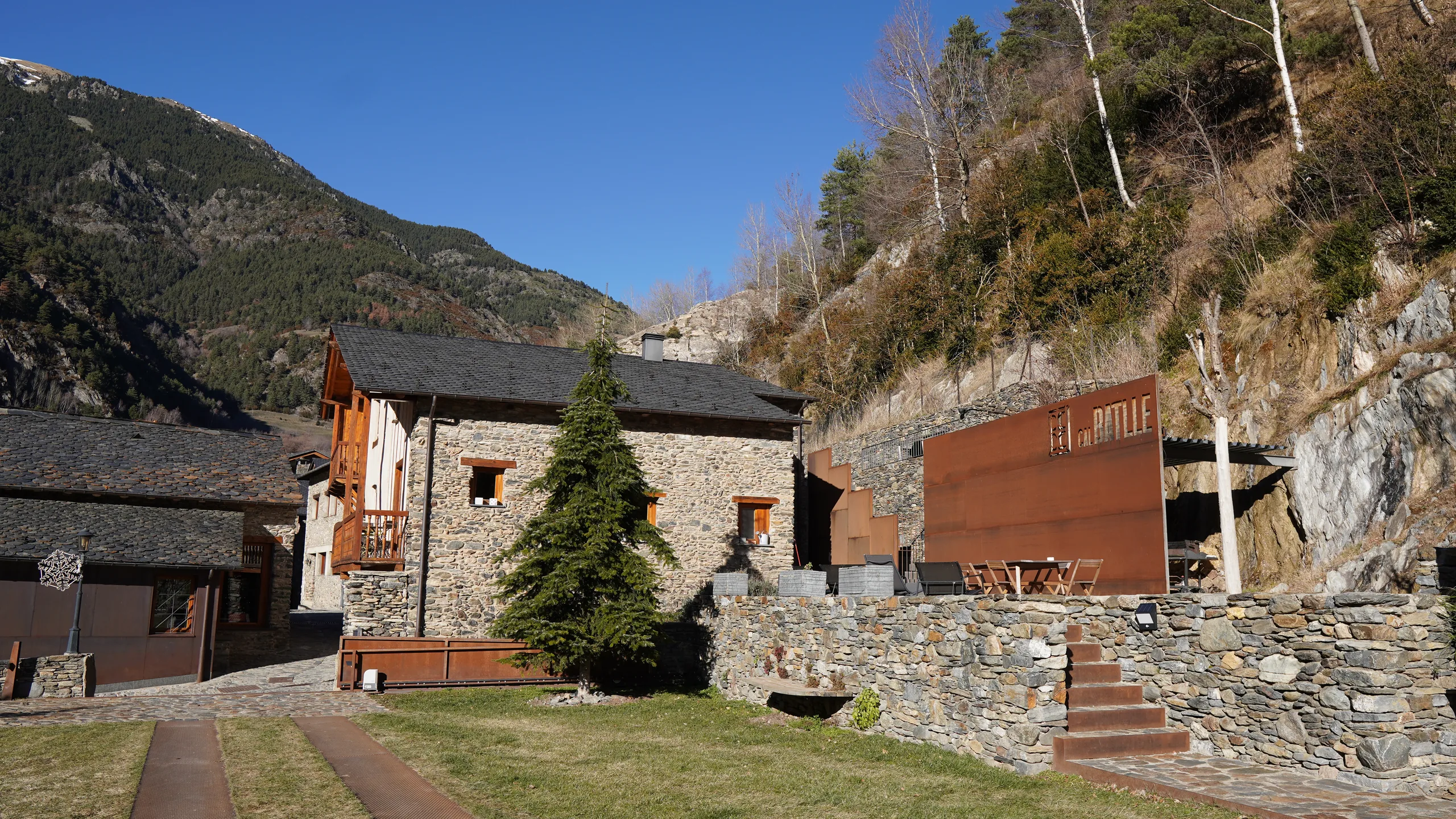 Façana de pedra de Cal Batlle amb el jardí i la muntanya al fons