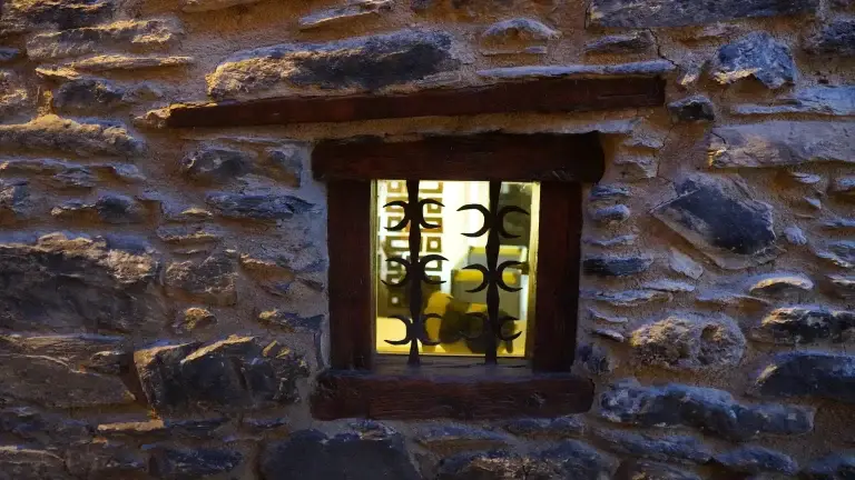 Finestra amb reixa de ferro en una paret de pedra, il·luminada de nit