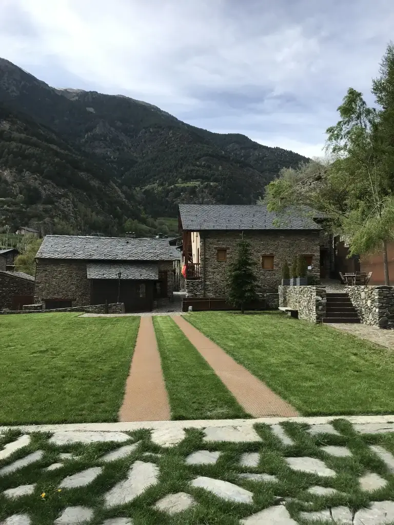 Jardí amb camins i les cases de pedra de Cal Batlle sota la muntanya