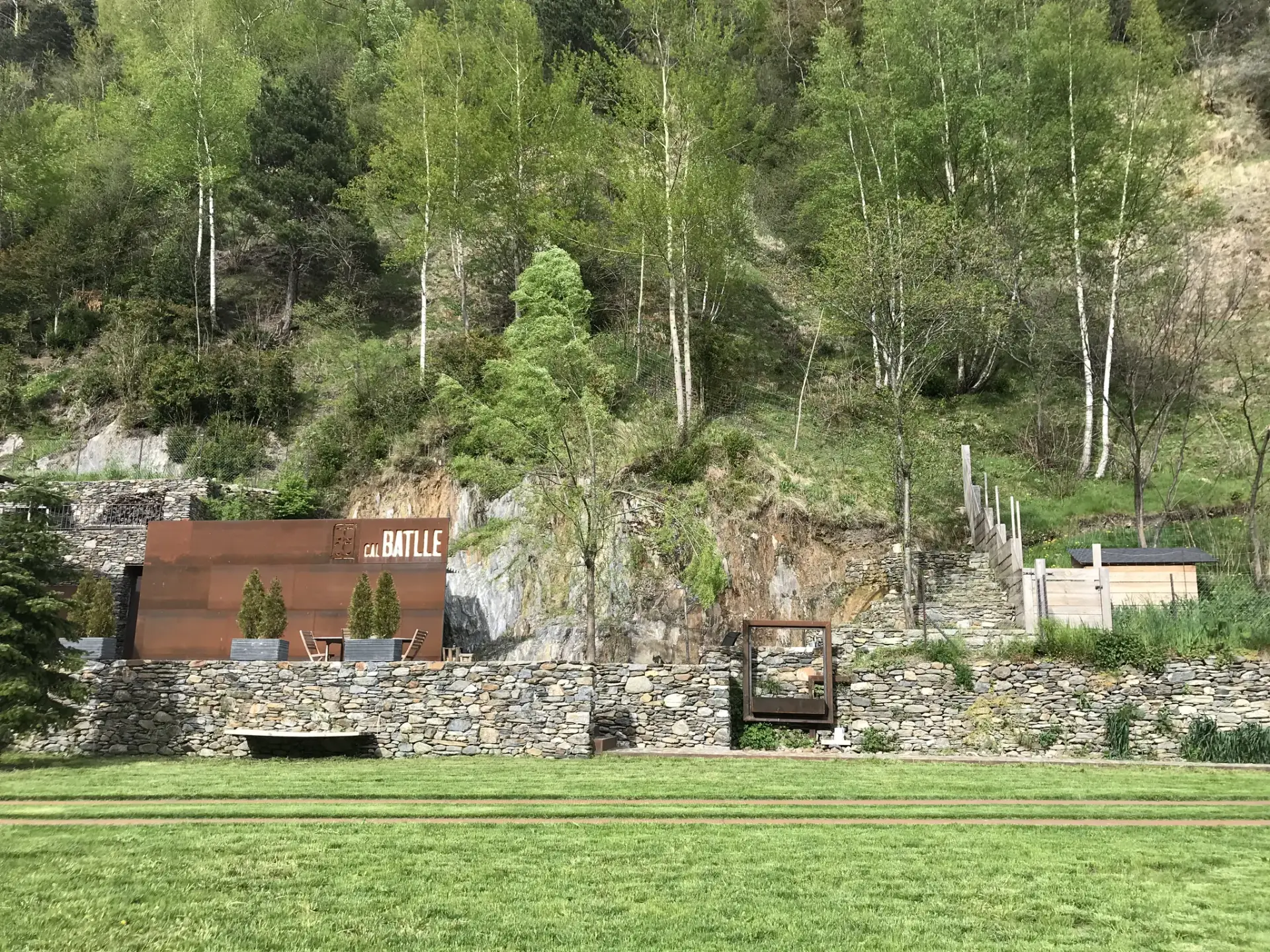 Jardí i murs de pedra seca de Cal Batlle amb la paret d'acer corten al peu del bosc
